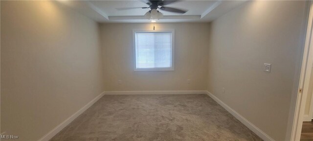 unfurnished room featuring ceiling fan, light colored carpet, and a tray ceiling