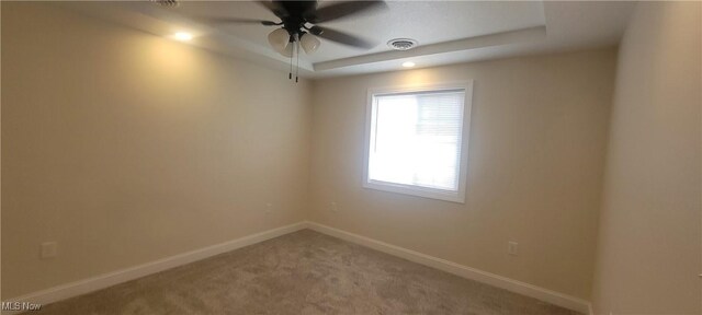 carpeted empty room with a tray ceiling and ceiling fan