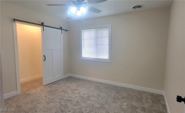 spare room with a barn door, light carpet, and ceiling fan