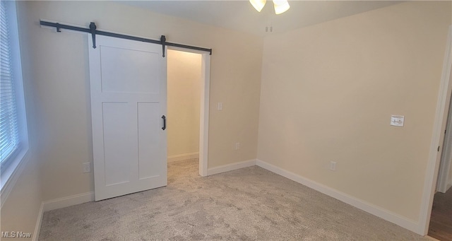 unfurnished bedroom with a barn door and light carpet