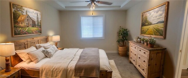 bedroom with ceiling fan, light colored carpet, and a tray ceiling