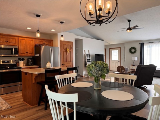 dining room with ceiling fan with notable chandelier, light wood-type flooring, a textured ceiling, and vaulted ceiling