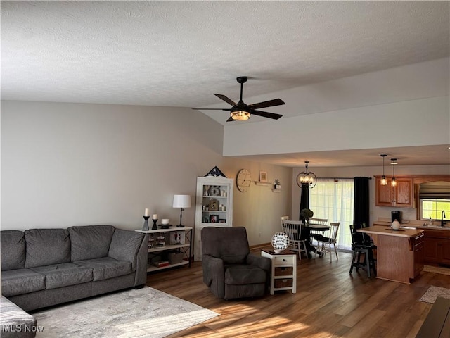 living room featuring lofted ceiling, ceiling fan with notable chandelier, sink, a textured ceiling, and dark hardwood / wood-style flooring