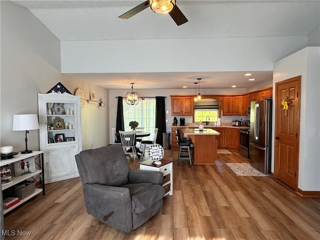 living room with ceiling fan with notable chandelier, wood-type flooring, sink, and vaulted ceiling