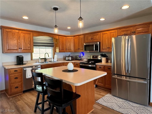 kitchen with sink, a center island, a textured ceiling, a breakfast bar, and appliances with stainless steel finishes