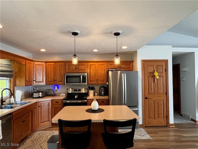 kitchen with sink, a center island, stainless steel appliances, pendant lighting, and a textured ceiling