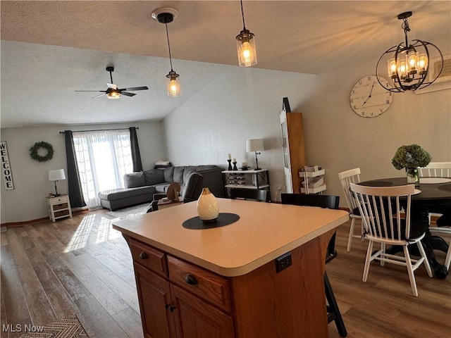 kitchen with ceiling fan with notable chandelier, a kitchen island, dark hardwood / wood-style floors, and vaulted ceiling