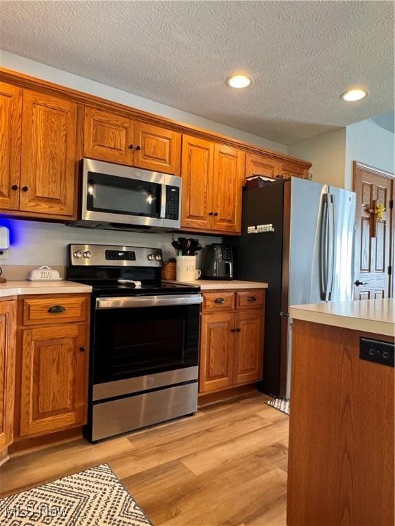 kitchen with light hardwood / wood-style floors, a textured ceiling, and appliances with stainless steel finishes