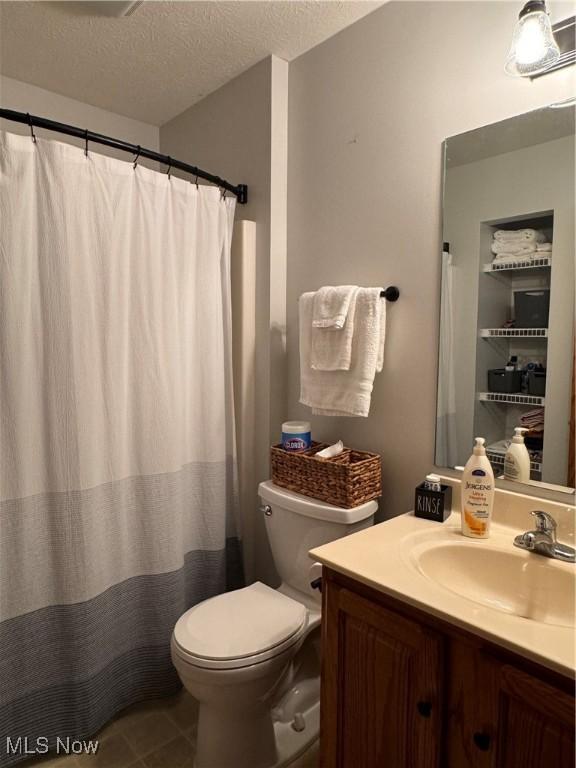 bathroom featuring walk in shower, vanity, a textured ceiling, tile patterned flooring, and toilet