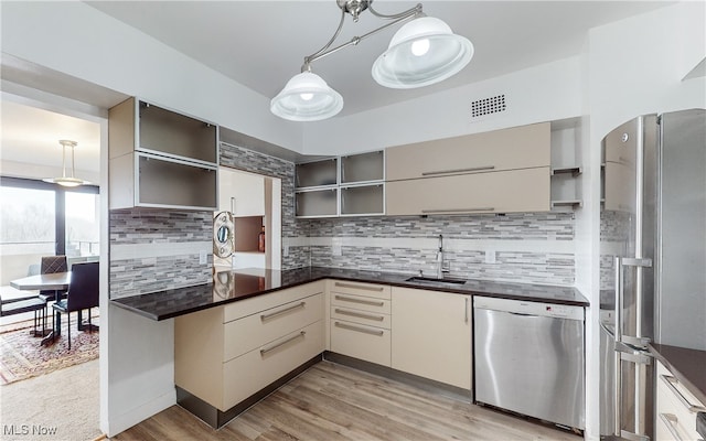 kitchen with light wood-type flooring, pendant lighting, stainless steel appliances, sink, and decorative backsplash