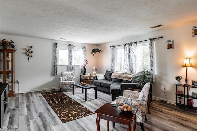 living area featuring light wood-type flooring, visible vents, and a textured ceiling