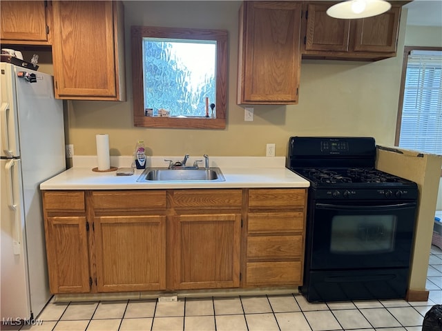 kitchen featuring gas stove, a healthy amount of sunlight, sink, light tile patterned flooring, and white fridge