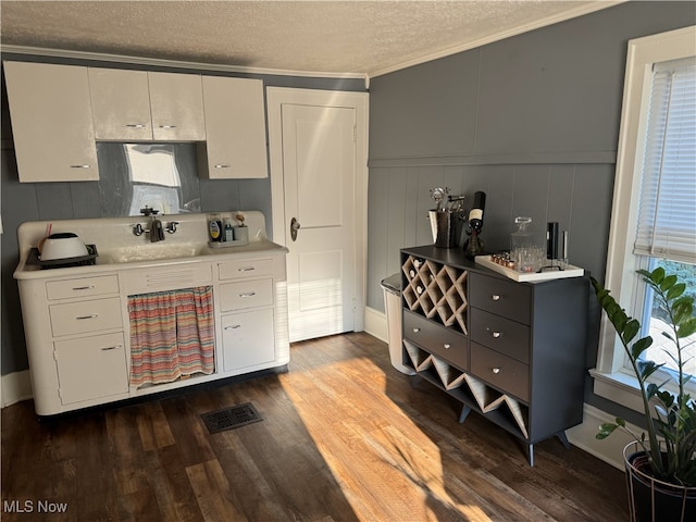 kitchen with a textured ceiling, dark hardwood / wood-style flooring, white cabinetry, crown molding, and sink