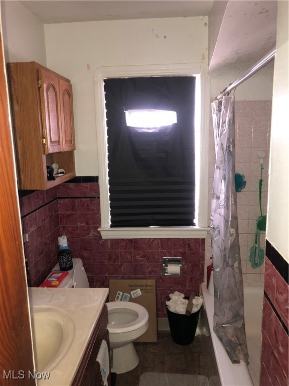 full bathroom with toilet, tile patterned floors, shower / bath combo with shower curtain, tile walls, and vanity