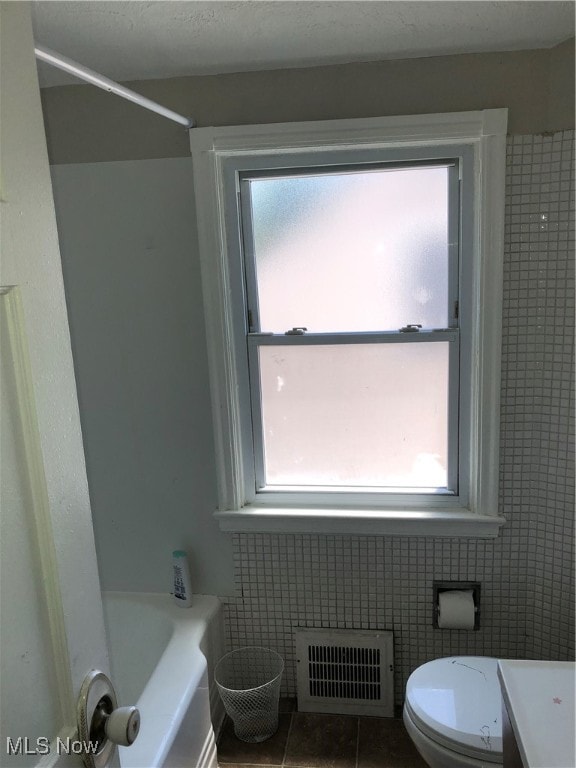 bathroom with tile walls, toilet, tile patterned flooring, and a wealth of natural light