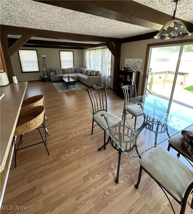 dining room with beamed ceiling, light wood-style floors, and a textured ceiling