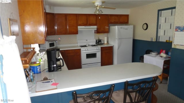 kitchen with kitchen peninsula, white appliances, a breakfast bar area, and ceiling fan