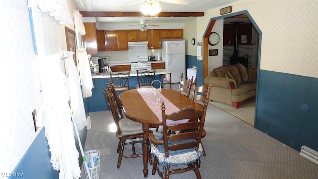 dining room with light carpet, beam ceiling, ceiling fan, and a wood stove