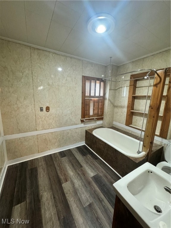 bathroom featuring a bathing tub, tile walls, wood-type flooring, ornamental molding, and vanity