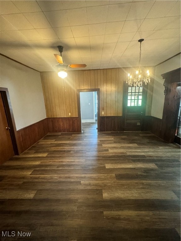 unfurnished room with wood walls, ceiling fan with notable chandelier, and hardwood / wood-style floors