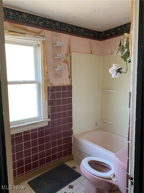 bathroom with washtub / shower combination, plenty of natural light, tile patterned floors, and toilet