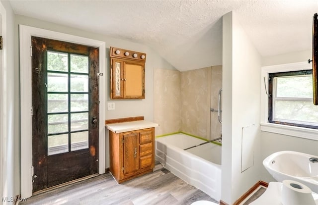 bathroom with wood-type flooring, a textured ceiling, vaulted ceiling, and vanity