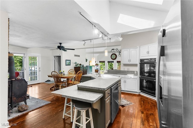 kitchen featuring white cabinetry, appliances with stainless steel finishes, a skylight, a center island with sink, and sink