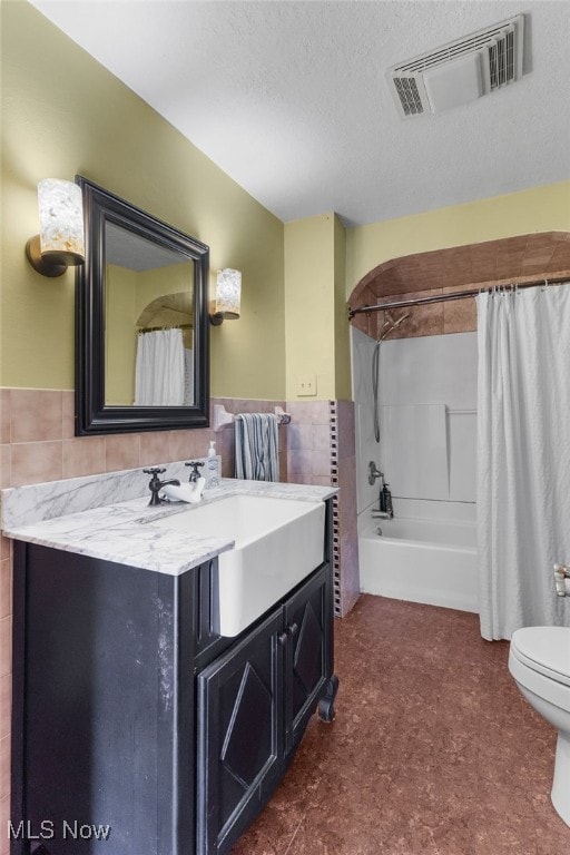 full bathroom featuring shower / tub combo with curtain, toilet, tile walls, a textured ceiling, and vanity