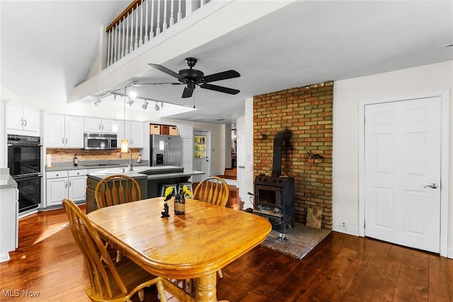 dining area with hardwood / wood-style floors, track lighting, ceiling fan, a wood stove, and brick wall