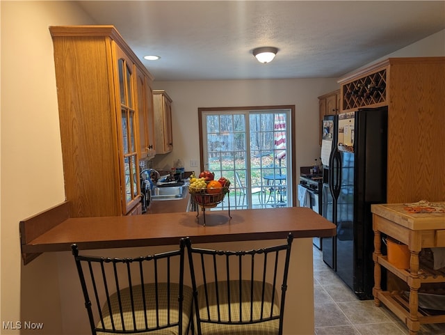 kitchen with a kitchen bar, kitchen peninsula, black fridge with ice dispenser, and sink