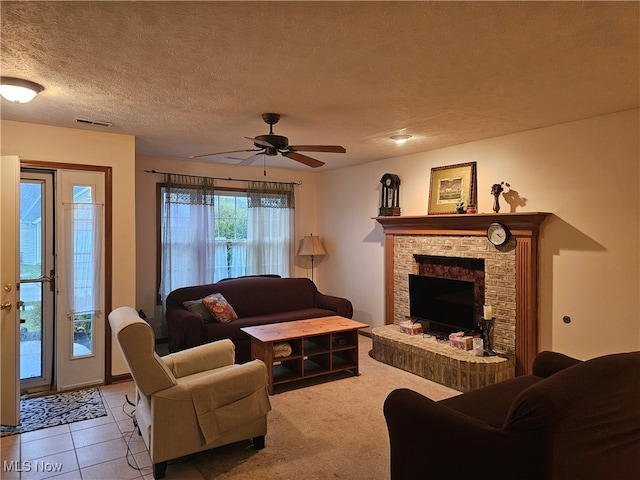 tiled living room featuring a stone fireplace, ceiling fan, and a textured ceiling