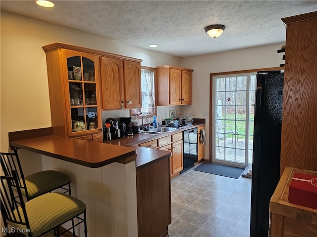 kitchen featuring black appliances, sink, a textured ceiling, kitchen peninsula, and a breakfast bar area