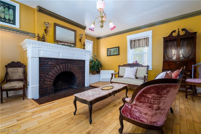 living room with an inviting chandelier, crown molding, a brick fireplace, and light hardwood / wood-style floors