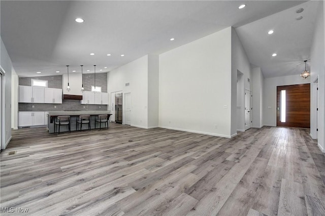 unfurnished living room featuring high vaulted ceiling and light hardwood / wood-style flooring