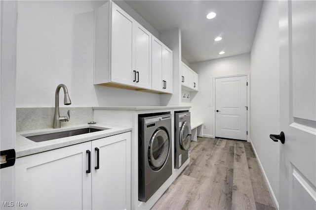 clothes washing area with cabinets, separate washer and dryer, sink, and light hardwood / wood-style flooring