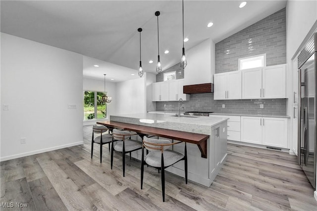 kitchen with white cabinetry, hanging light fixtures, light wood-type flooring, and a center island with sink