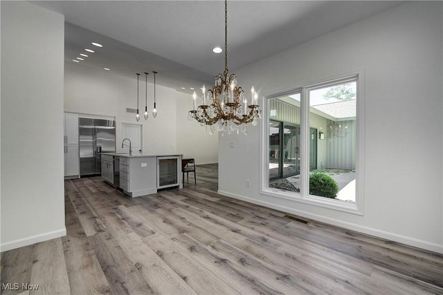 unfurnished dining area featuring wine cooler, sink, an inviting chandelier, and light wood-type flooring