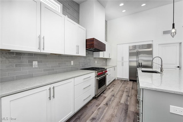 kitchen featuring sink, decorative light fixtures, premium appliances, light stone countertops, and white cabinets