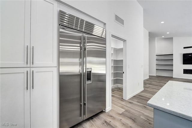 kitchen featuring white cabinetry, stainless steel built in refrigerator, light stone countertops, and light hardwood / wood-style flooring