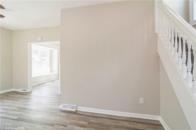 interior space with light wood-style flooring, a ceiling fan, visible vents, stairs, and baseboards