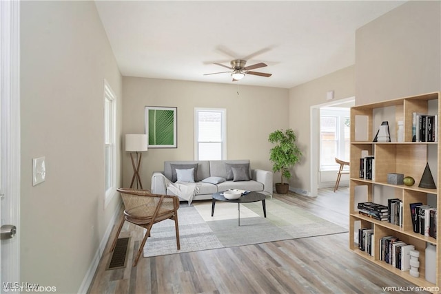 living room with light wood-style floors, baseboards, visible vents, and a ceiling fan