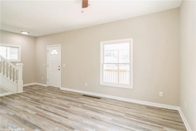 spare room with baseboards, stairway, visible vents, and light wood-style floors