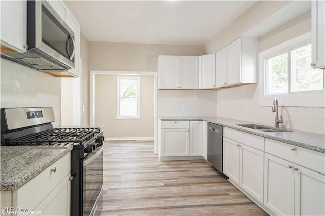 kitchen featuring a sink, white cabinetry, light wood-style floors, appliances with stainless steel finishes, and light stone countertops