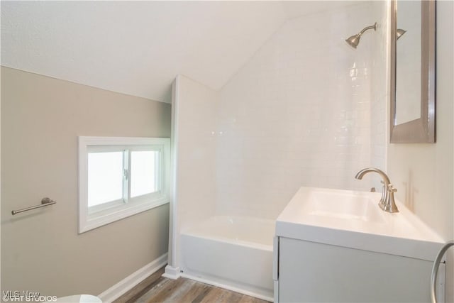 bathroom featuring baseboards, bathing tub / shower combination, wood finished floors, vaulted ceiling, and vanity