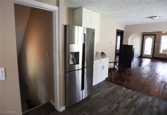 kitchen with a textured ceiling, white cabinets, light stone countertops, stainless steel fridge, and dark hardwood / wood-style flooring