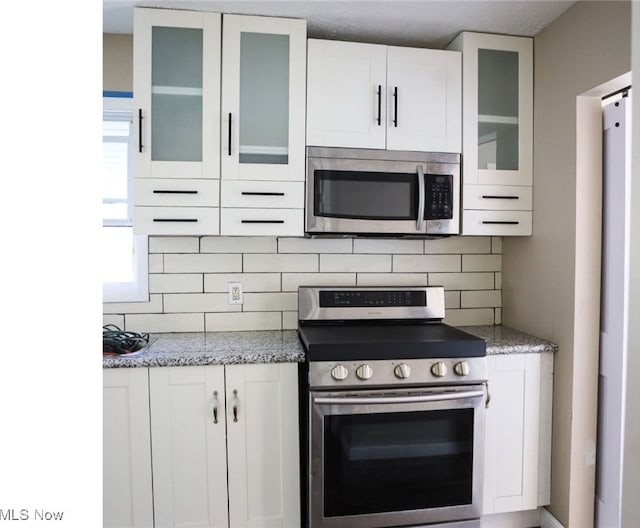 kitchen featuring appliances with stainless steel finishes, light stone countertops, tasteful backsplash, and white cabinetry