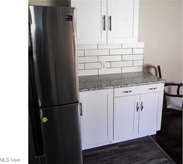 kitchen featuring decorative backsplash, white cabinets, stainless steel refrigerator, dark wood-type flooring, and stone countertops