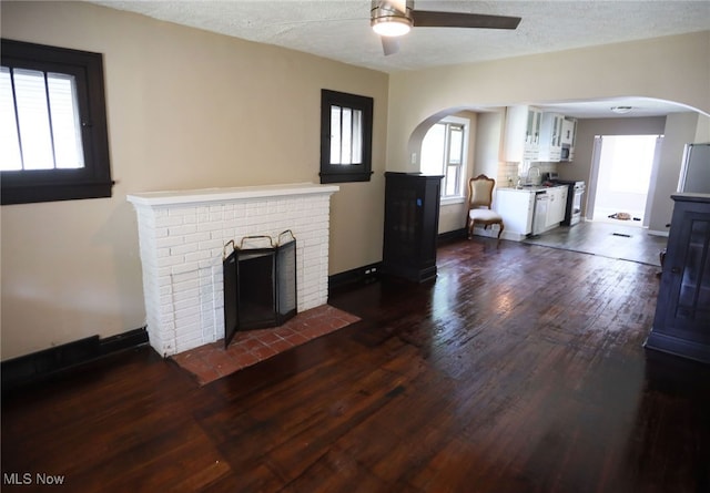 unfurnished living room with ceiling fan, a brick fireplace, dark hardwood / wood-style floors, and a healthy amount of sunlight