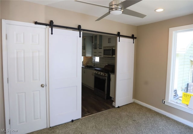 interior space with dark hardwood / wood-style flooring, range, ceiling fan, decorative backsplash, and a barn door