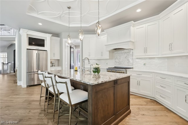 kitchen with white cabinets, light wood-type flooring, custom exhaust hood, a tray ceiling, and stainless steel refrigerator